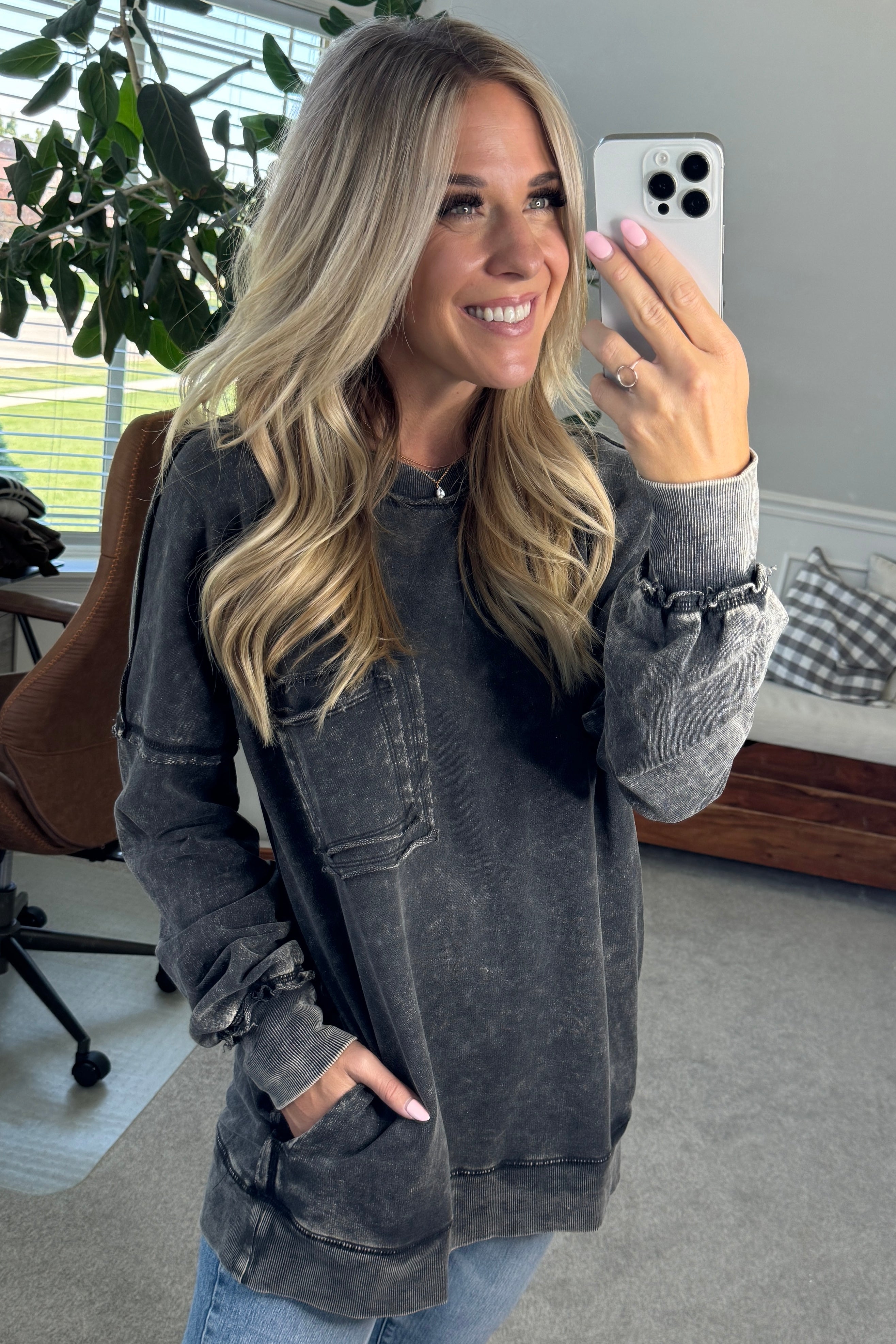 Blonde woman wearing a boyfriend fit drop shoulder sweatshirt pullover, with front pocket accent, exposed raw seams, and all over acid wash detail.