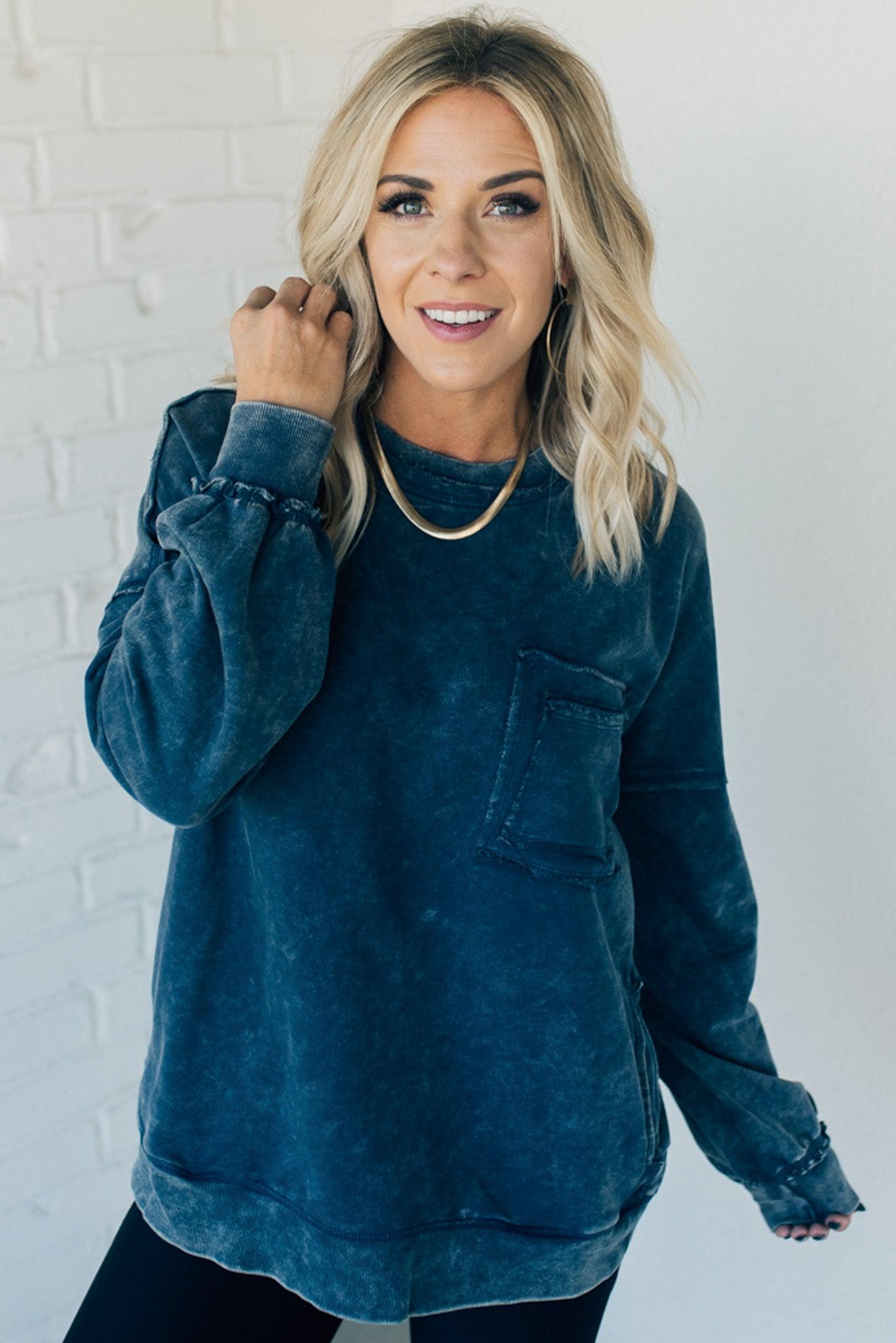 Blonde woman wearing a boyfriend fit drop shoulder sweatshirt pullover, with front pocket accent, exposed raw seams, and all over acid wash detail.