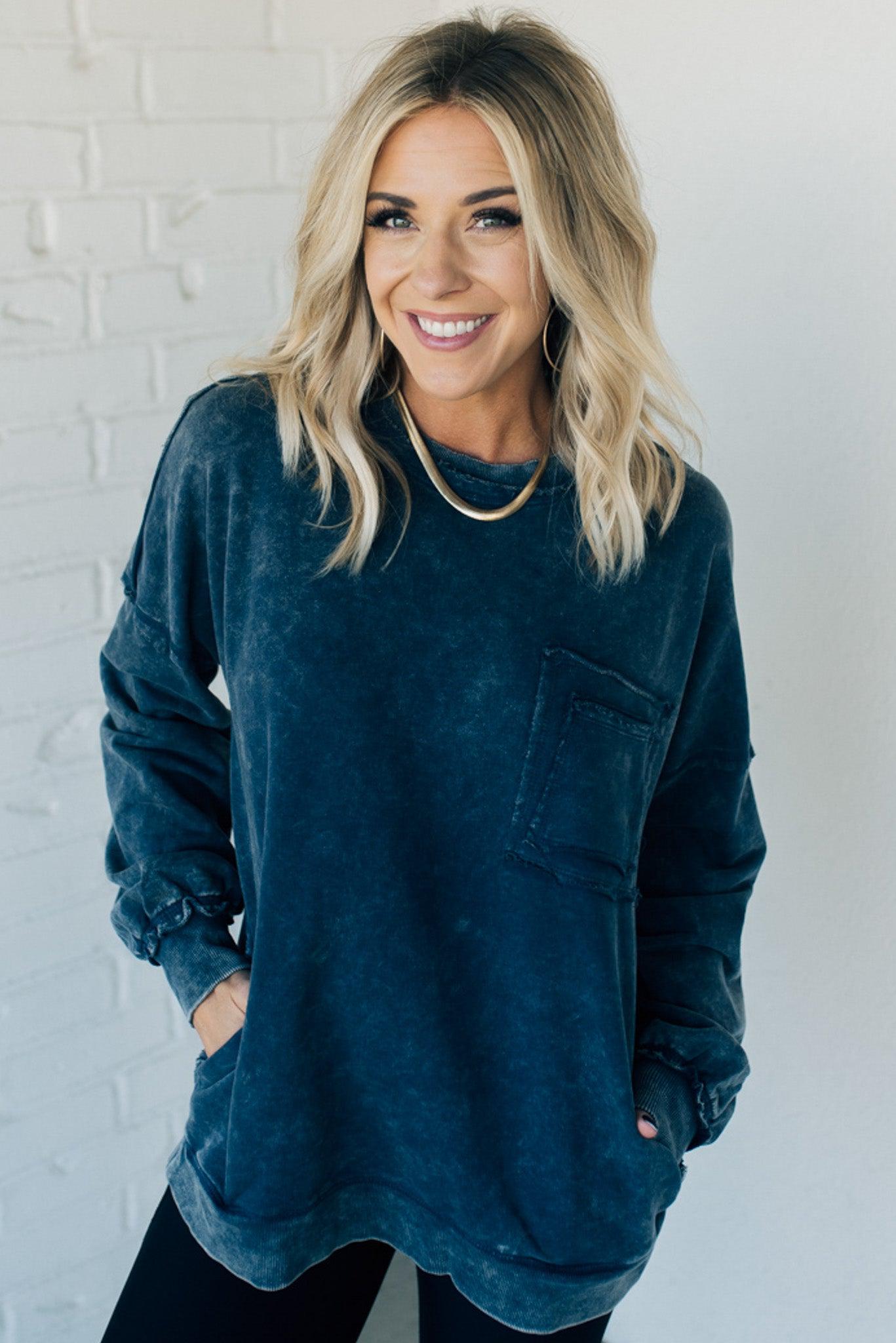 Blonde woman wearing a boyfriend fit drop shoulder sweatshirt pullover, with front pocket accent, exposed raw seams, and all over acid wash detail.