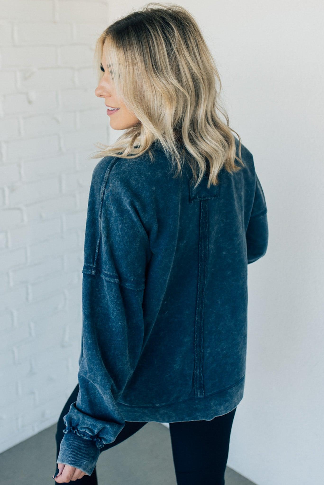 Blonde woman wearing a boyfriend fit drop shoulder sweatshirt pullover, with front pocket accent, exposed raw seams, and all over acid wash detail.