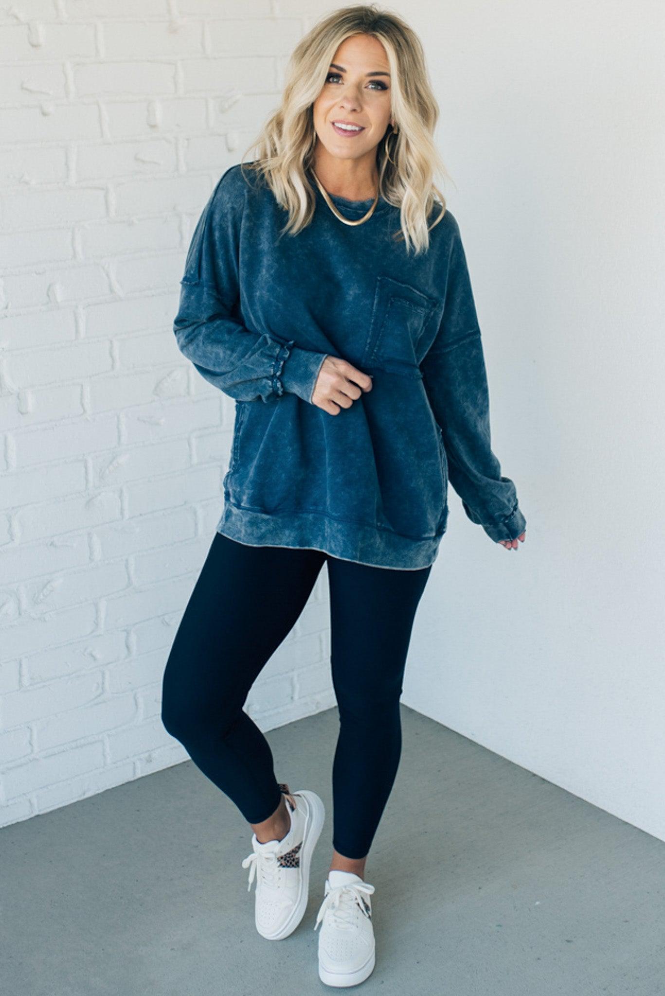 Blonde woman wearing a boyfriend fit drop shoulder sweatshirt pullover, with front pocket accent, exposed raw seams, and all over acid wash detail.