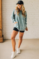 Blonde woman wearing a boyfriend fit drop shoulder sweatshirt pullover, with front pocket accent, exposed raw seams, and all over acid wash detail.