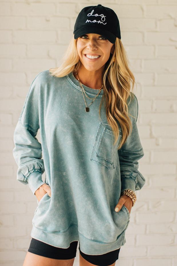 Blonde woman wearing a boyfriend fit drop shoulder sweatshirt pullover, with front pocket accent, exposed raw seams, and all over acid wash detail.