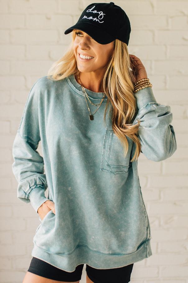 Blonde woman wearing a boyfriend fit drop shoulder sweatshirt pullover, with front pocket accent, exposed raw seams, and all over acid wash detail.