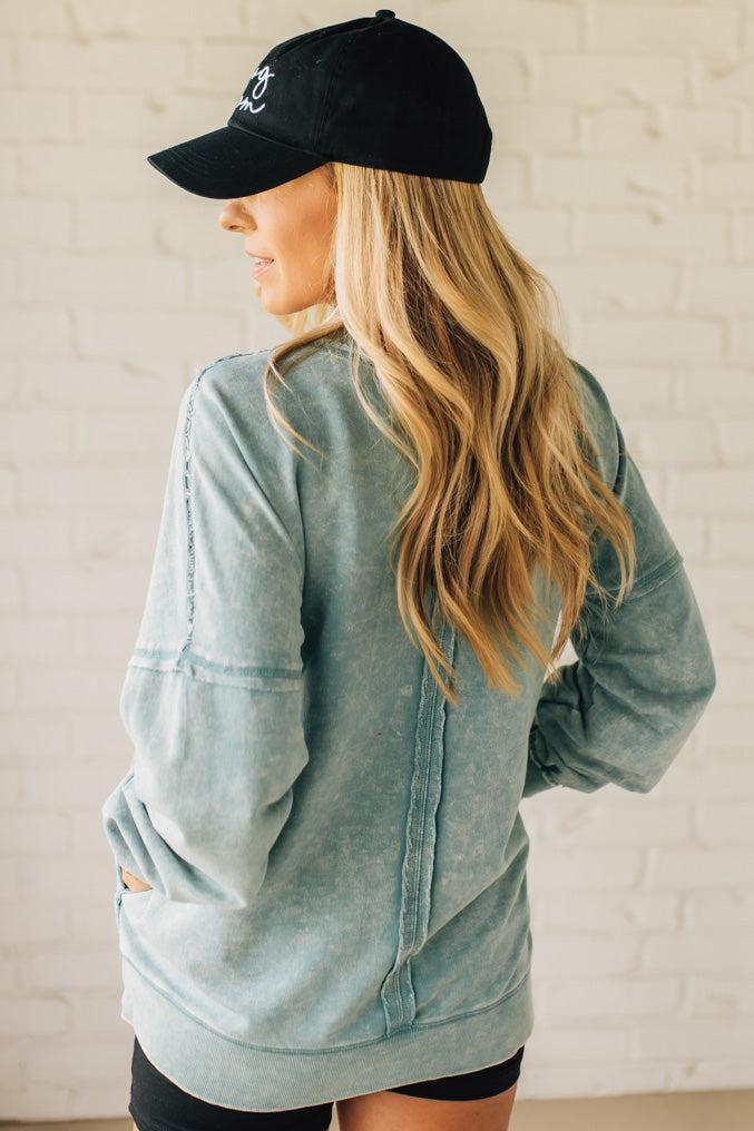 Blonde woman wearing a boyfriend fit drop shoulder sweatshirt pullover, with front pocket accent, exposed raw seams, and all over acid wash detail.