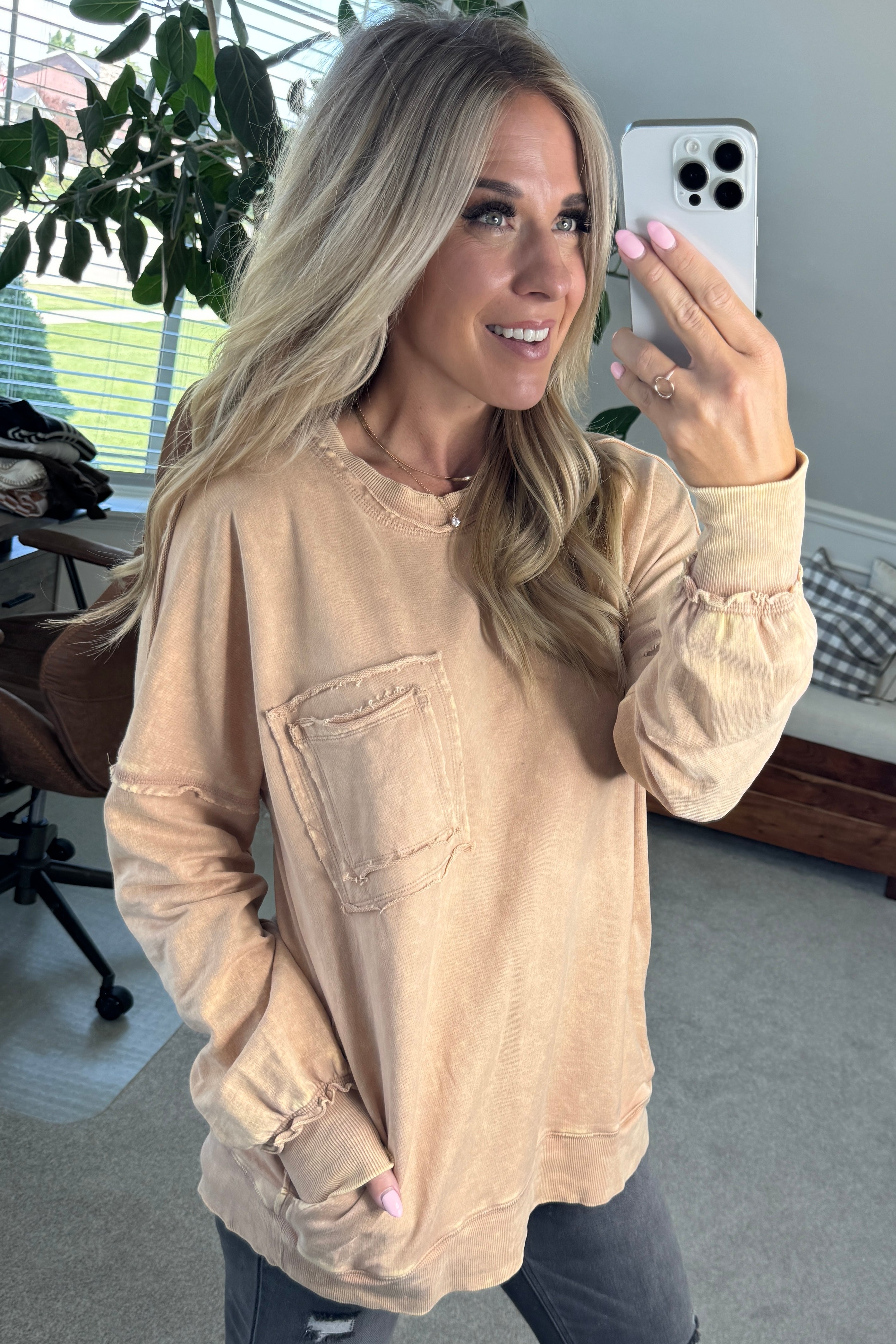 Blonde woman wearing a boyfriend fit drop shoulder sweatshirt pullover, with front pocket accent, exposed raw seams, and all over acid wash detail.