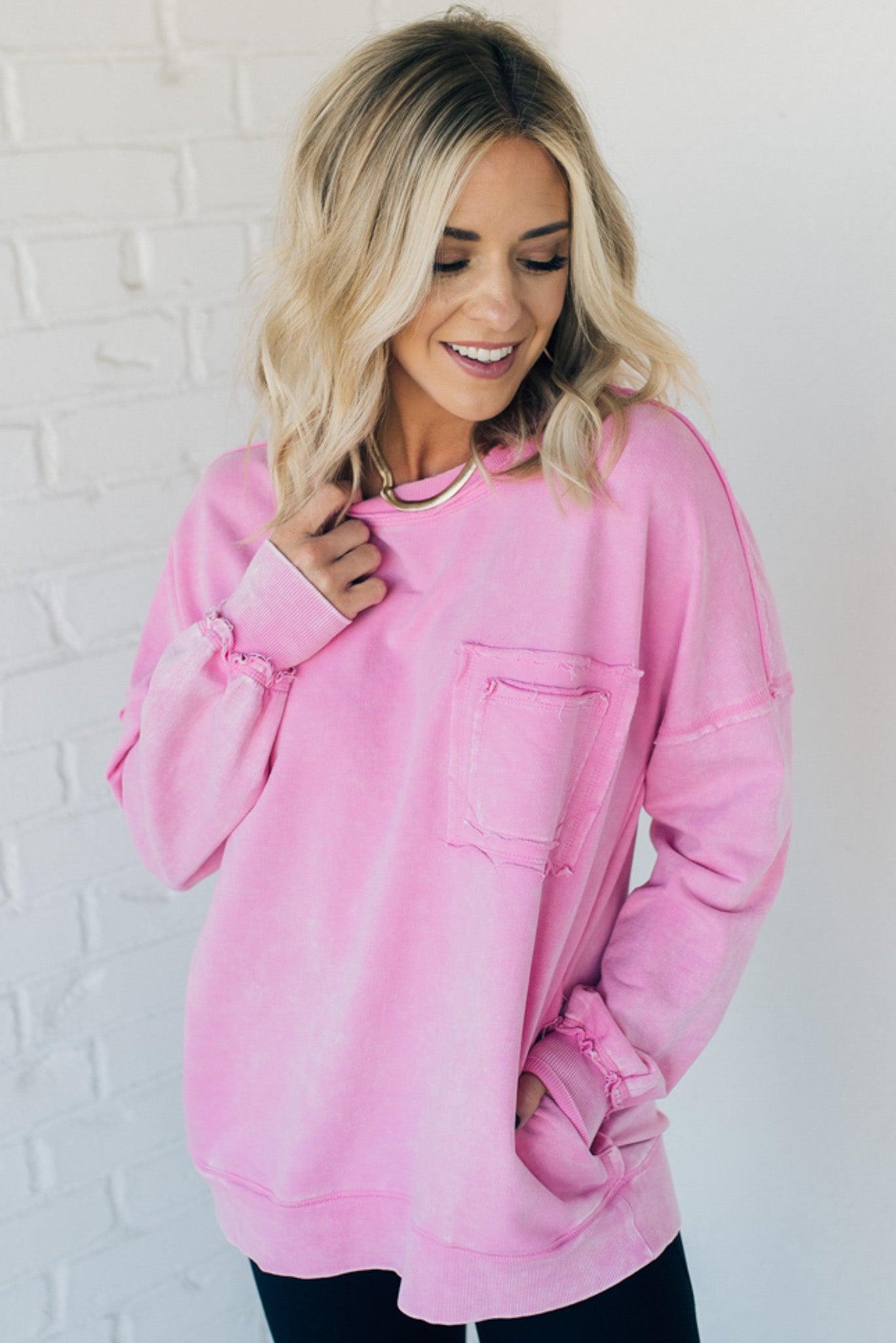 Blonde woman wearing a boyfriend fit drop shoulder sweatshirt pullover, with front pocket accent, exposed raw seams, and all over acid wash detail.