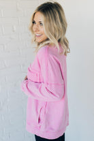 Blonde woman wearing a boyfriend fit drop shoulder sweatshirt pullover, with front pocket accent, exposed raw seams, and all over acid wash detail.