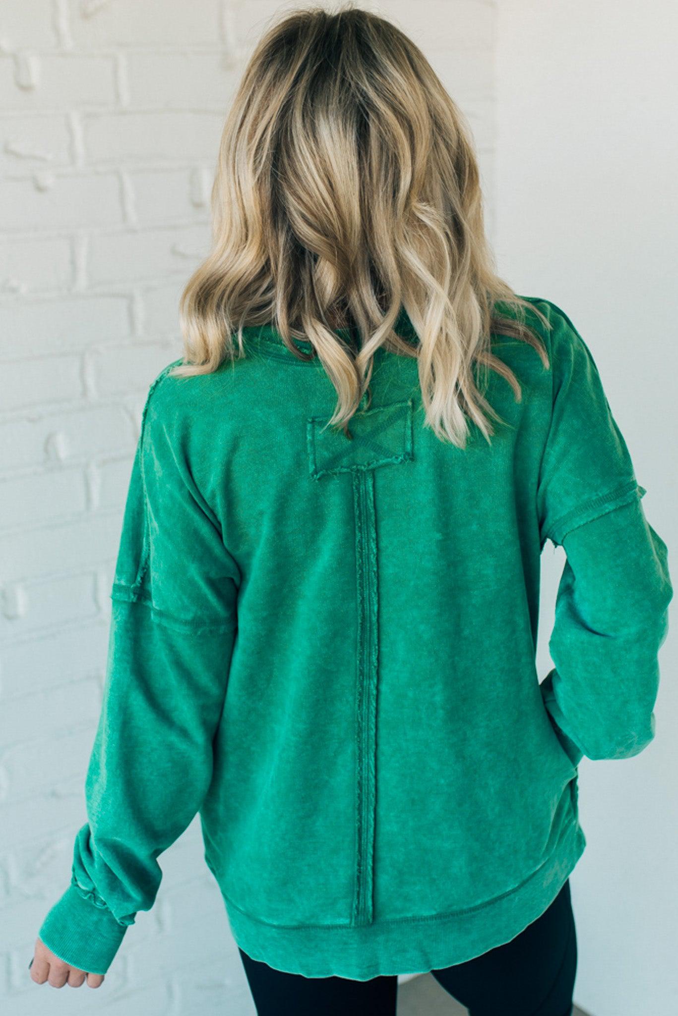 Blonde woman wearing a boyfriend fit drop shoulder sweatshirt pullover, with front pocket accent, exposed raw seams, and all over acid wash detail.