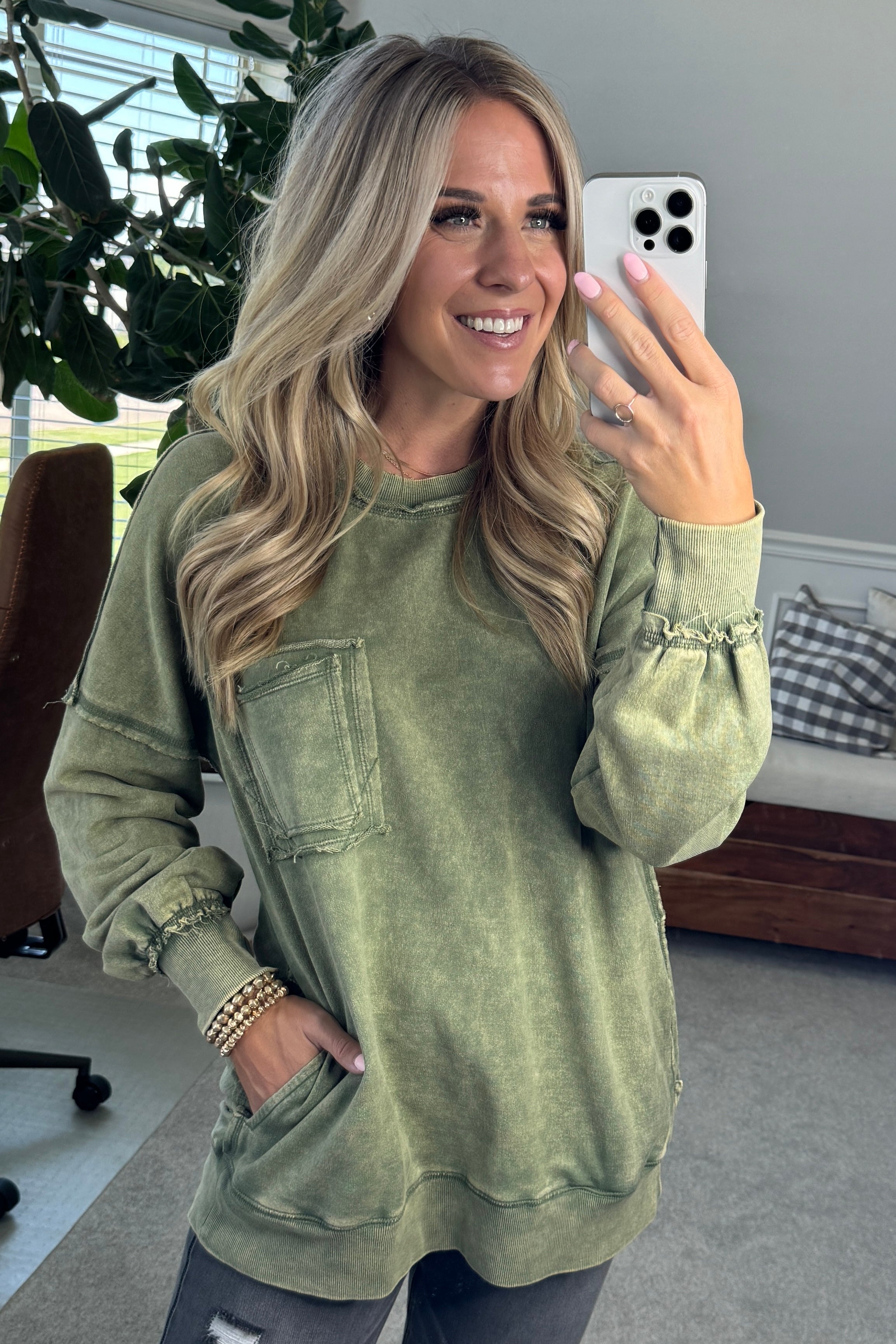 Blonde woman wearing a boyfriend fit drop shoulder sweatshirt pullover, with front pocket accent, exposed raw seams, and all over acid wash detail.