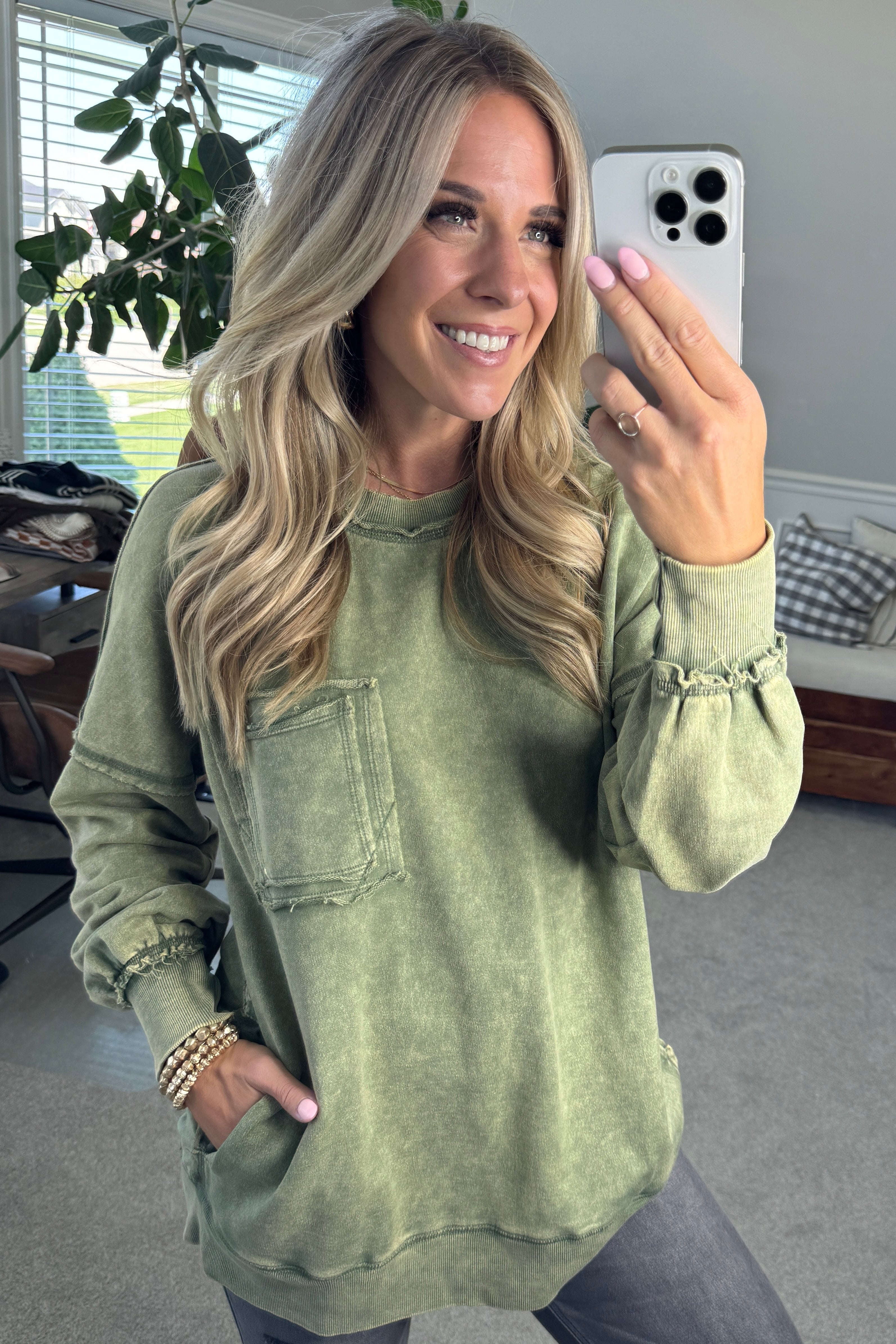 Blonde woman wearing a boyfriend fit drop shoulder sweatshirt pullover, with front pocket accent, exposed raw seams, and all over acid wash detail.