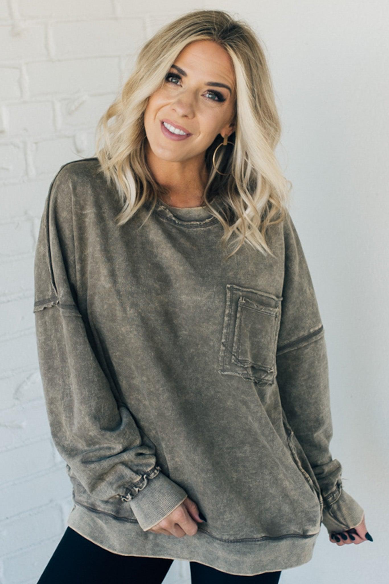 Blonde woman wearing a boyfriend fit drop shoulder sweatshirt pullover, with front pocket accent, exposed raw seams, and all over acid wash detail.