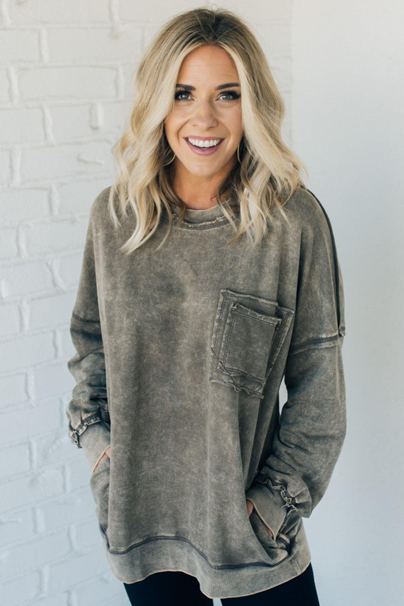 Blonde woman wearing a boyfriend fit drop shoulder sweatshirt pullover, with front pocket accent, exposed raw seams, and all over acid wash detail.