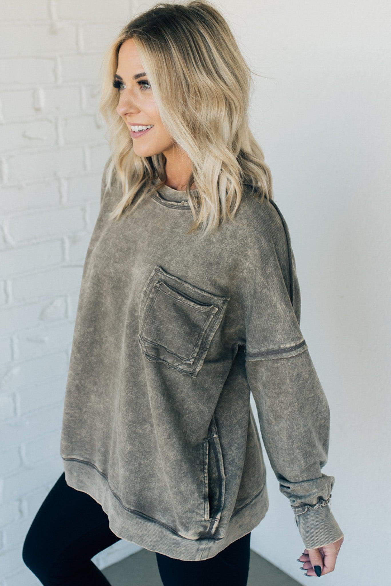 Blonde woman wearing a boyfriend fit drop shoulder sweatshirt pullover, with front pocket accent, exposed raw seams, and all over acid wash detail.