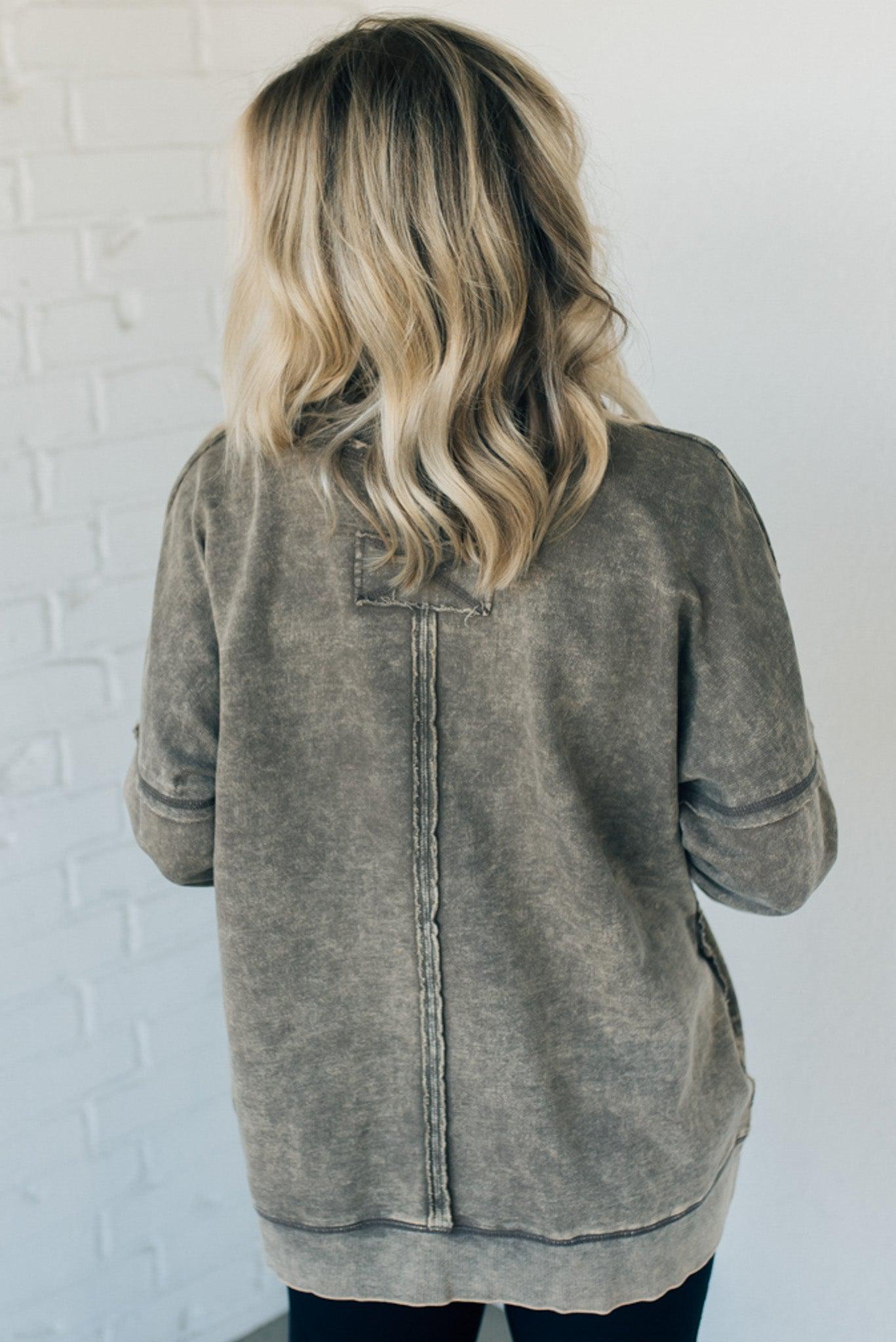 Blonde woman wearing a boyfriend fit drop shoulder sweatshirt pullover, with front pocket accent, exposed raw seams, and all over acid wash detail.