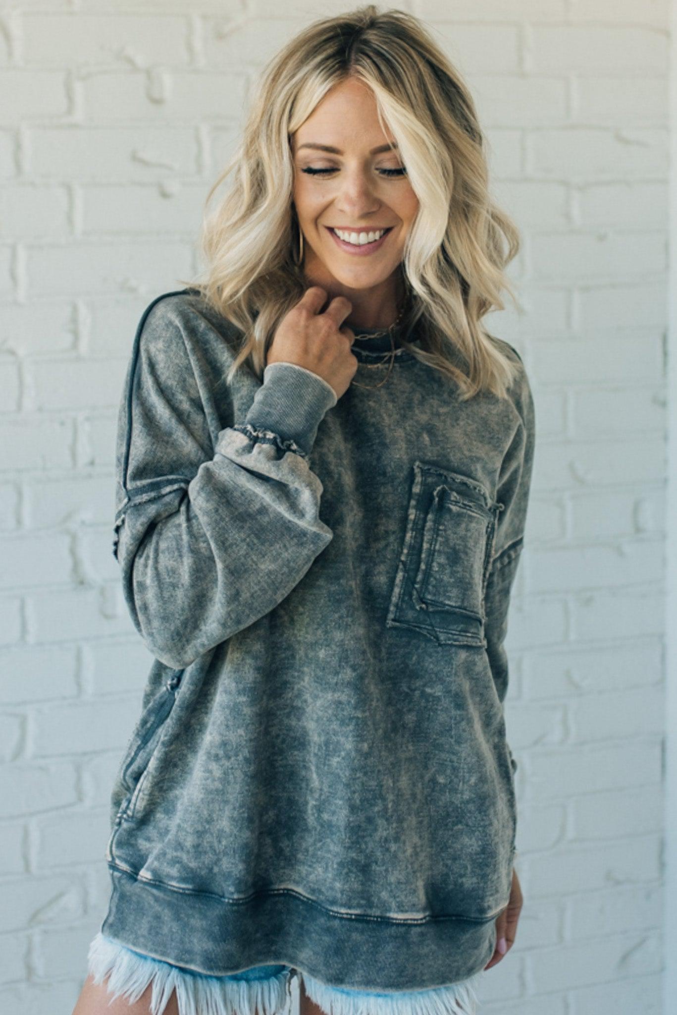 Blonde woman wearing a boyfriend fit drop shoulder sweatshirt pullover, with front pocket accent, exposed raw seams, and all over acid wash detail.