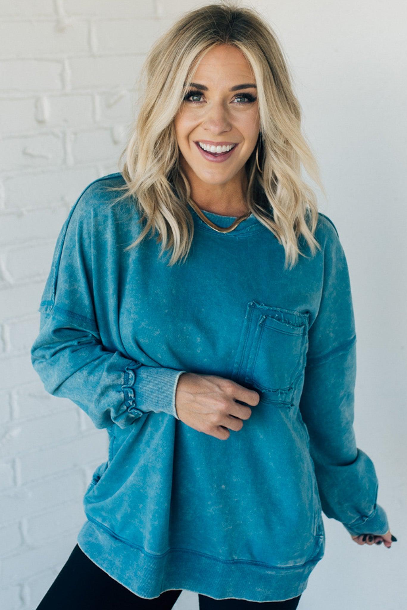Blonde woman wearing a boyfriend fit drop shoulder sweatshirt pullover, with front pocket accent, exposed raw seams, and all over acid wash detail.