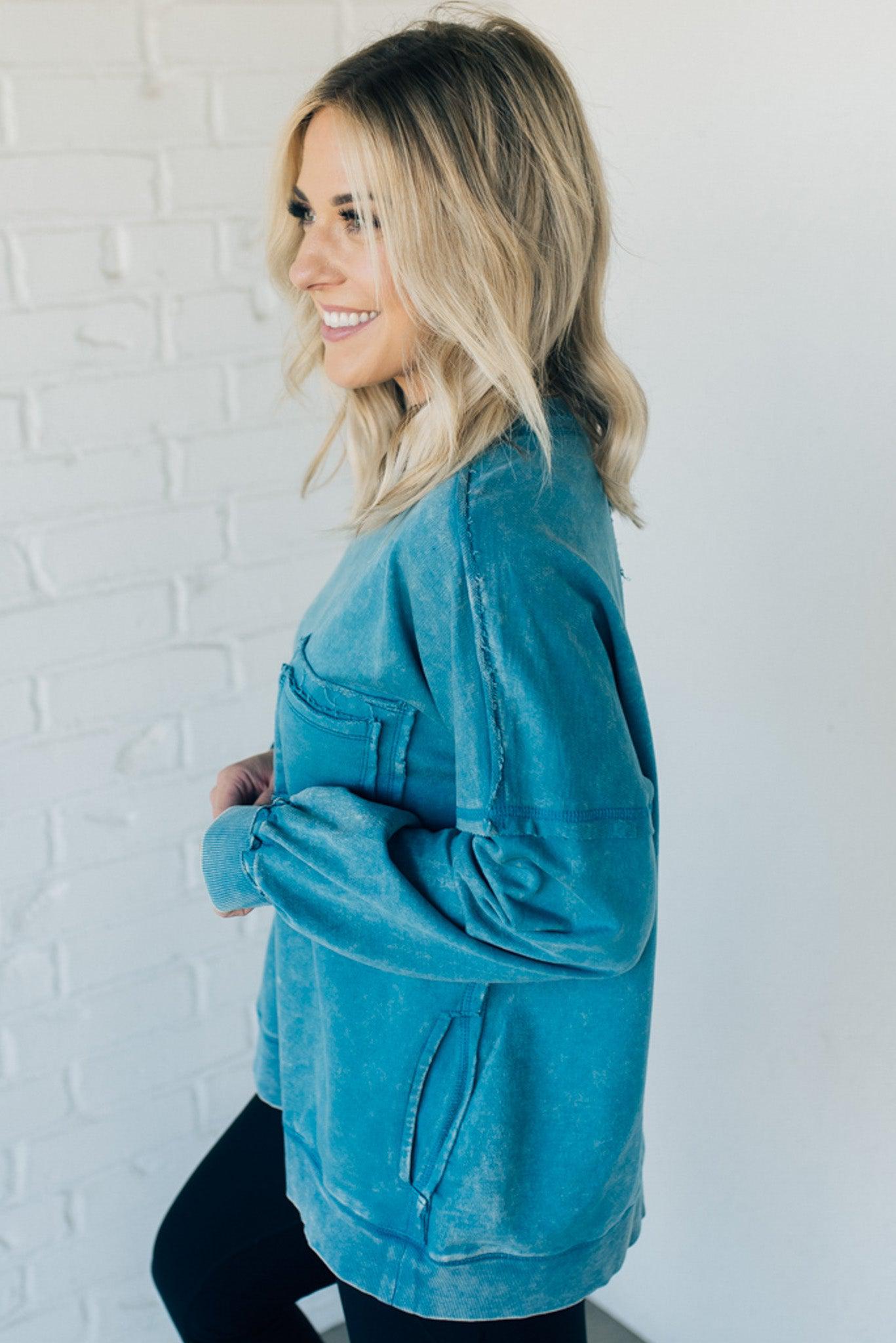 Blonde woman wearing a boyfriend fit drop shoulder sweatshirt pullover, with front pocket accent, exposed raw seams, and all over acid wash detail.