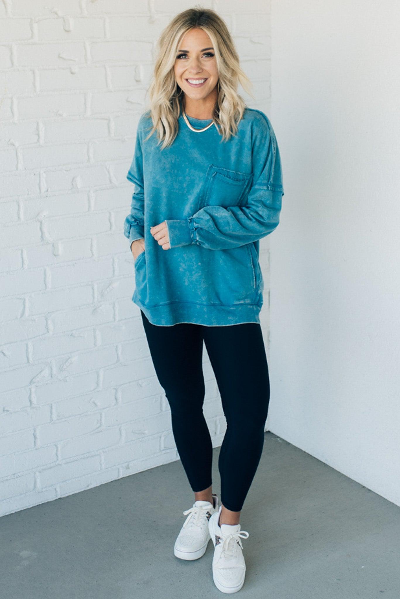 Blonde woman wearing a boyfriend fit drop shoulder sweatshirt pullover, with front pocket accent, exposed raw seams, and all over acid wash detail.