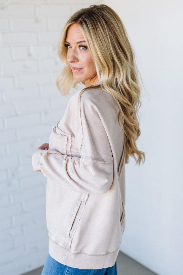 Woman wearing a beige jacket against a white brick wall