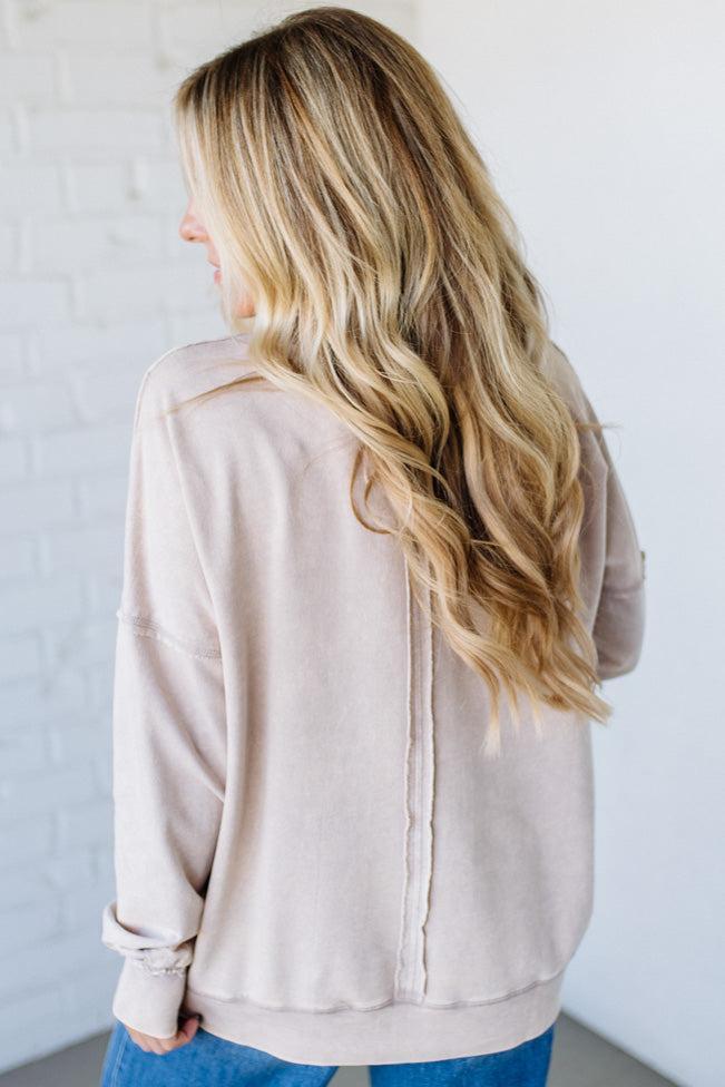 Person wearing a beige jacket with long blonde hair, standing against a plain background