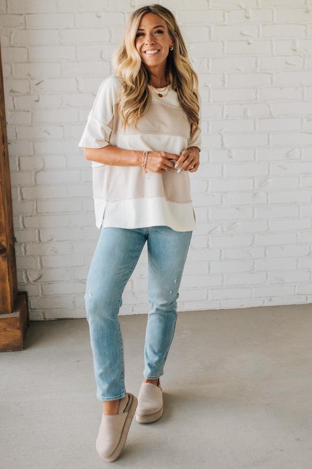 Woman wearing a white t-shirt and light blue jeans standing against a white brick wall.