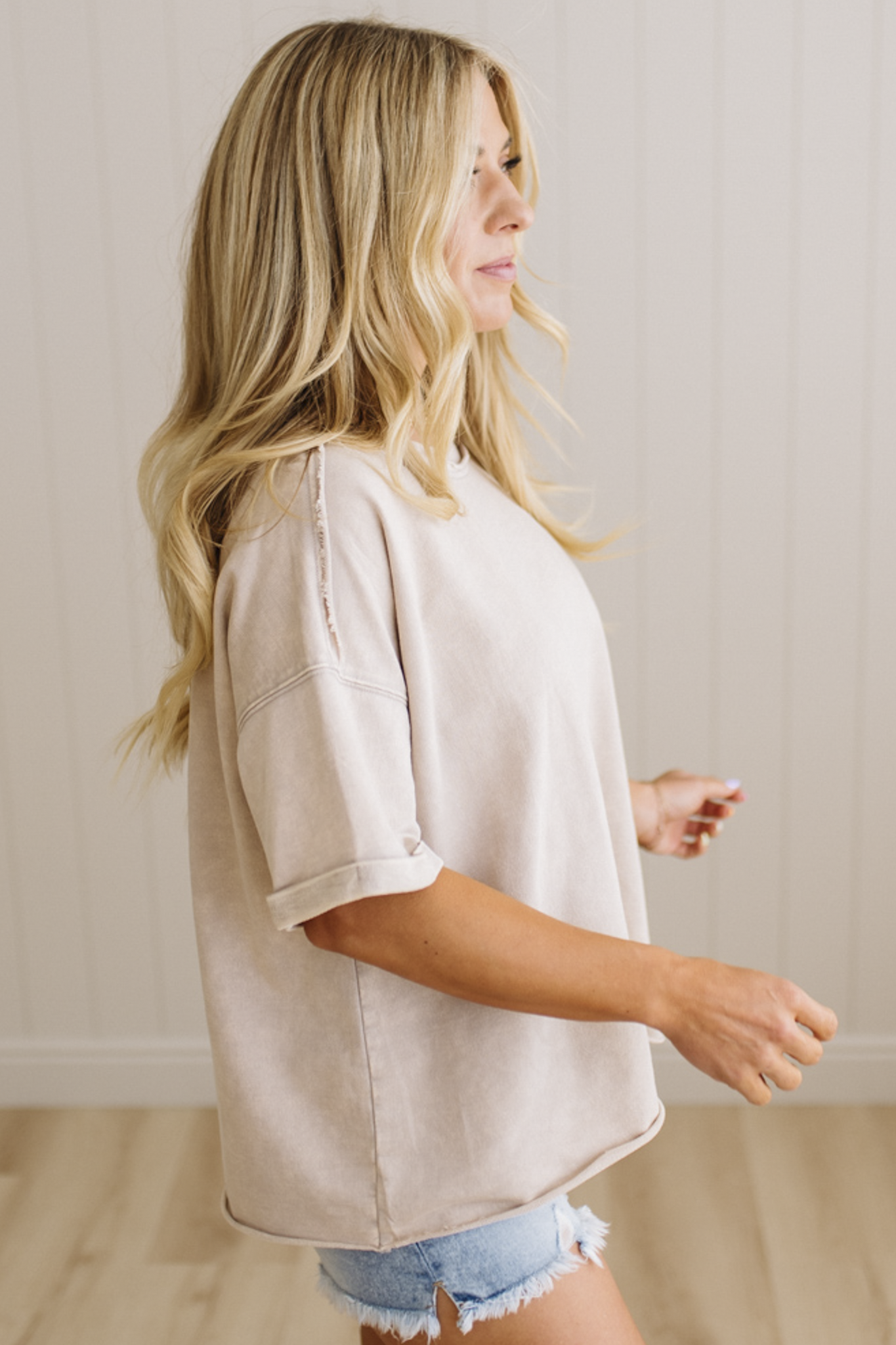 Woman wearing a beige oversized shirt and denim shorts in a neutral setting