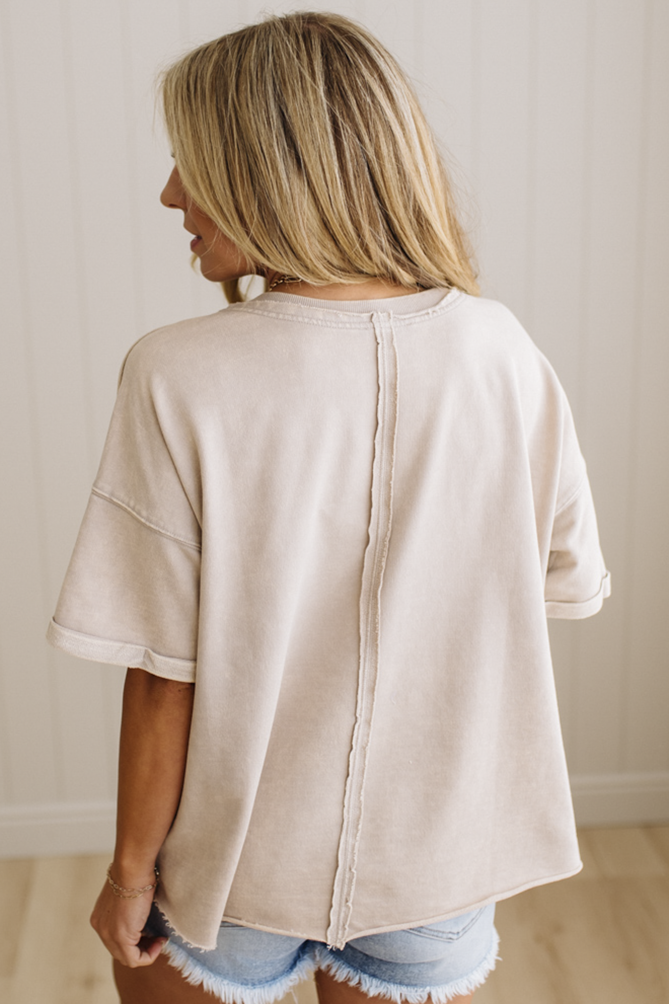 Person wearing a beige seam back top with denim shorts against a neutral background