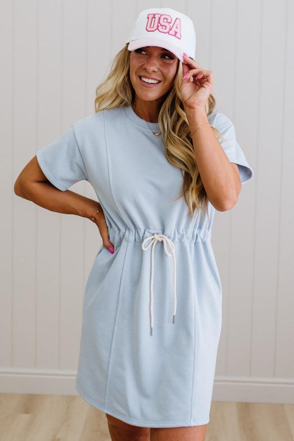 Woman wearing a light blue dress and white cap with 'USA' text against a plain background