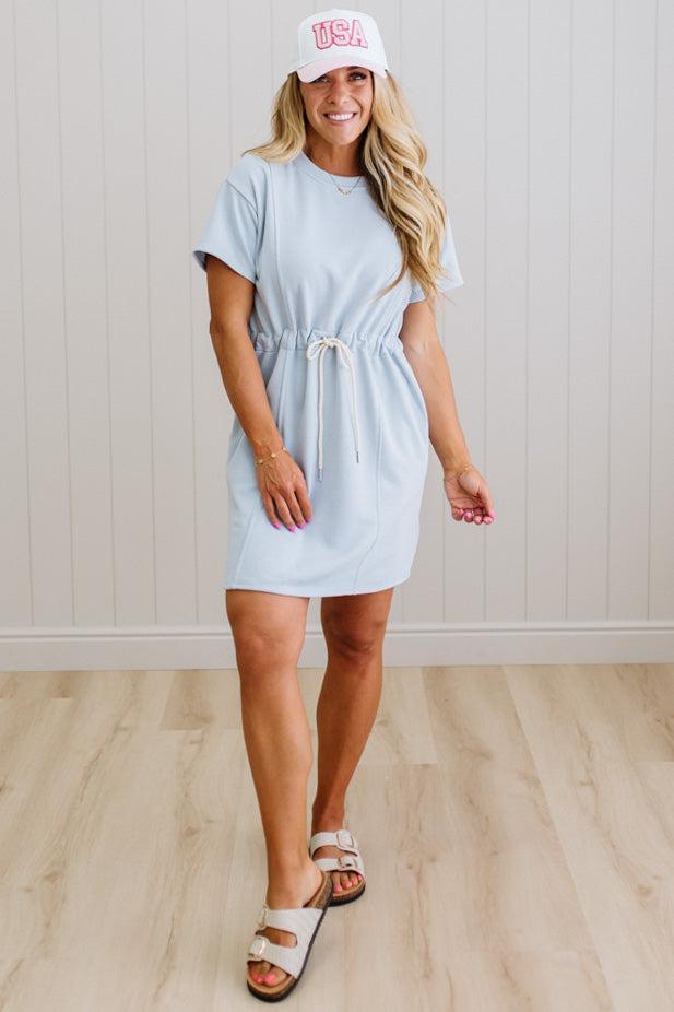 Woman wearing a light blue dress and white cap with 'USA' text on a wooden floor.