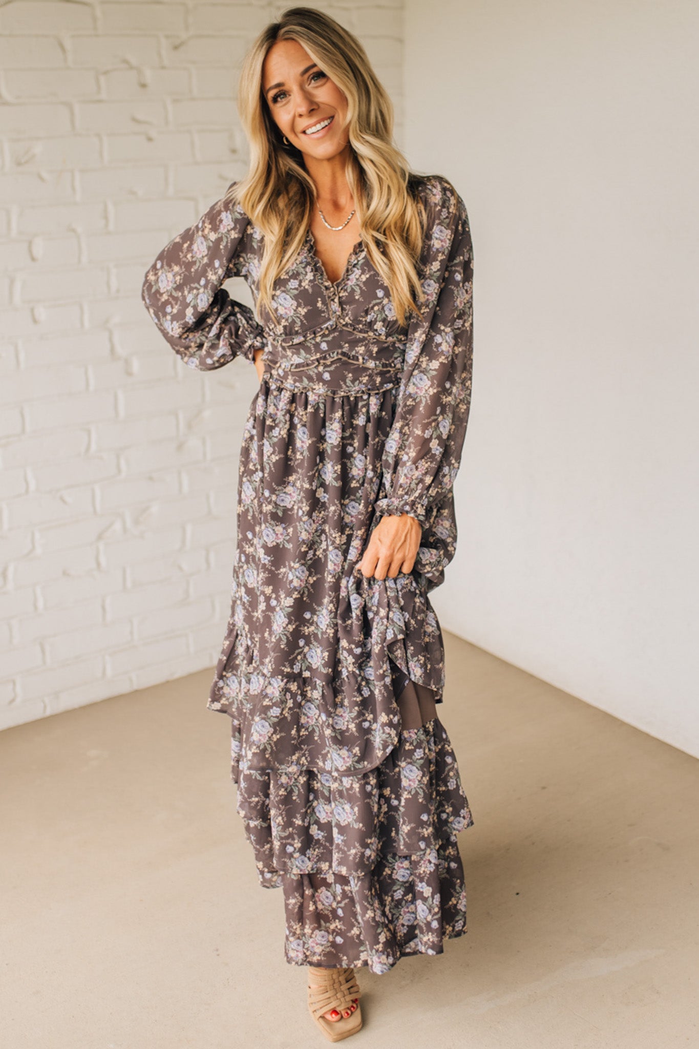 Woman wearing a floral dress standing against a white brick wall.