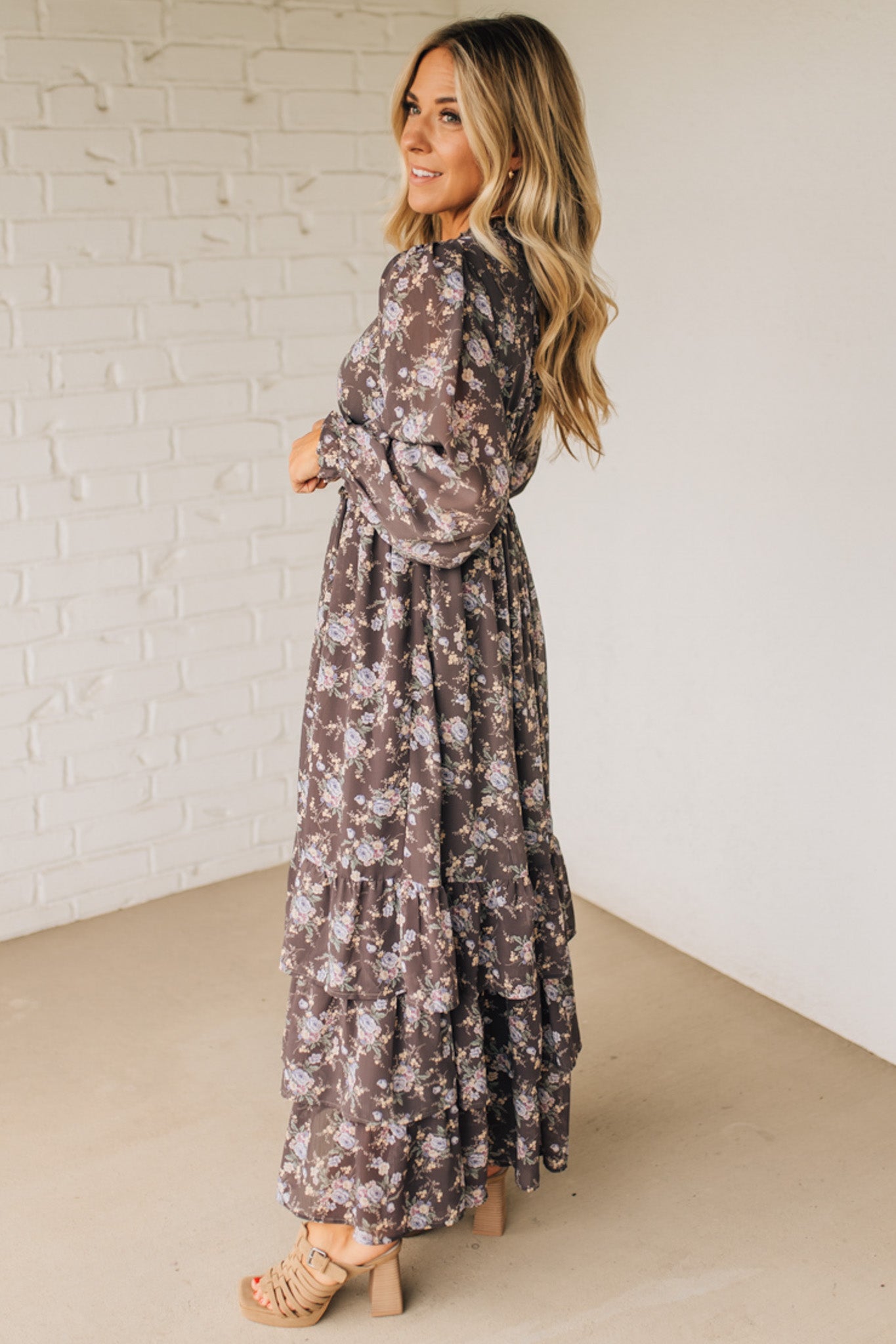 Woman wearing a floral dress standing against a white brick wall.