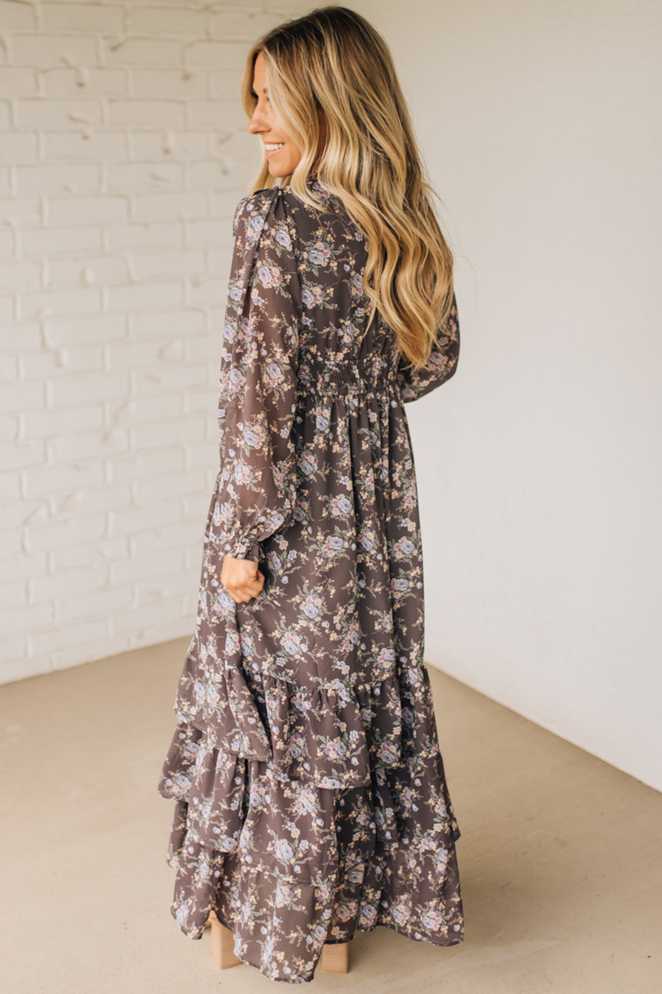 Woman wearing a floral dress against a white brick wall.