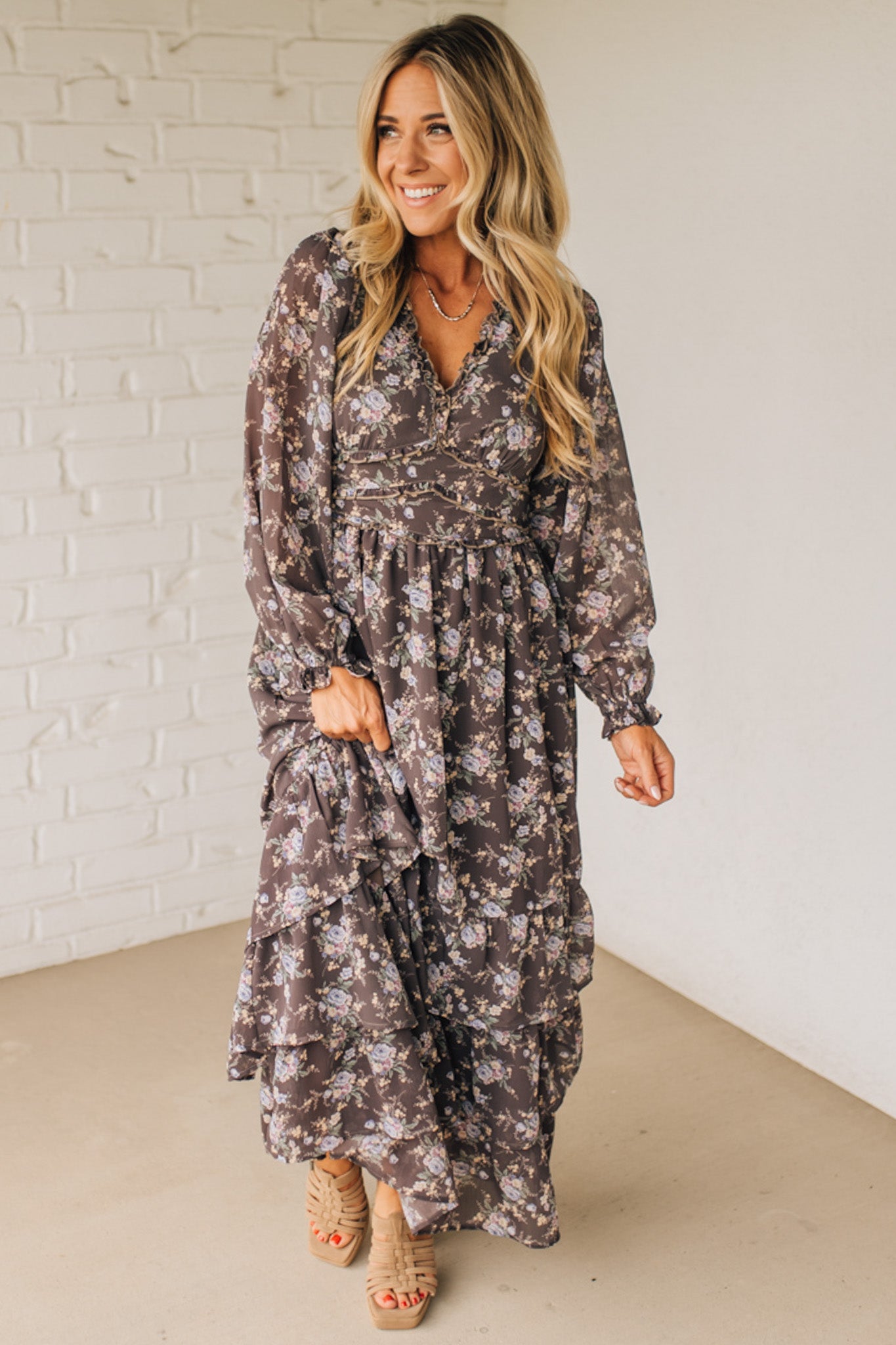 Woman wearing a floral dress against a white brick wall.