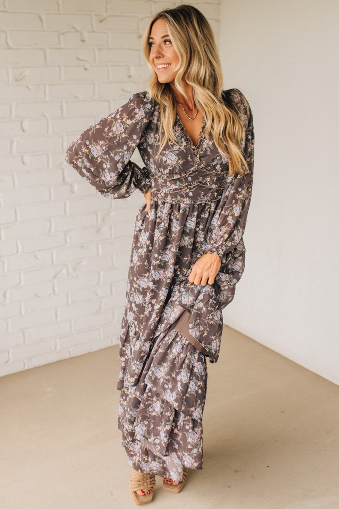 Woman wearing a floral dress standing against a white brick wall.