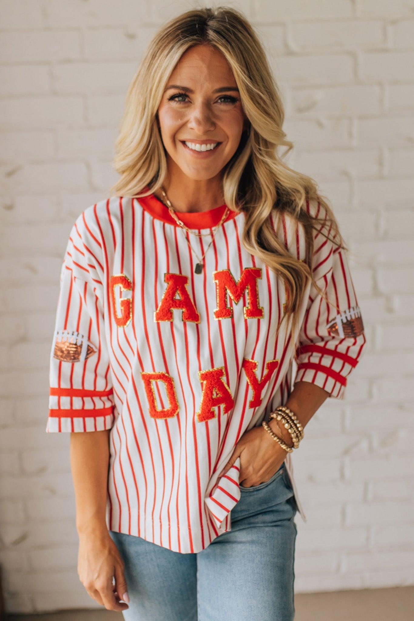 Woman wearing a 'GAMEDAY' striped shirt against a white brick wall.