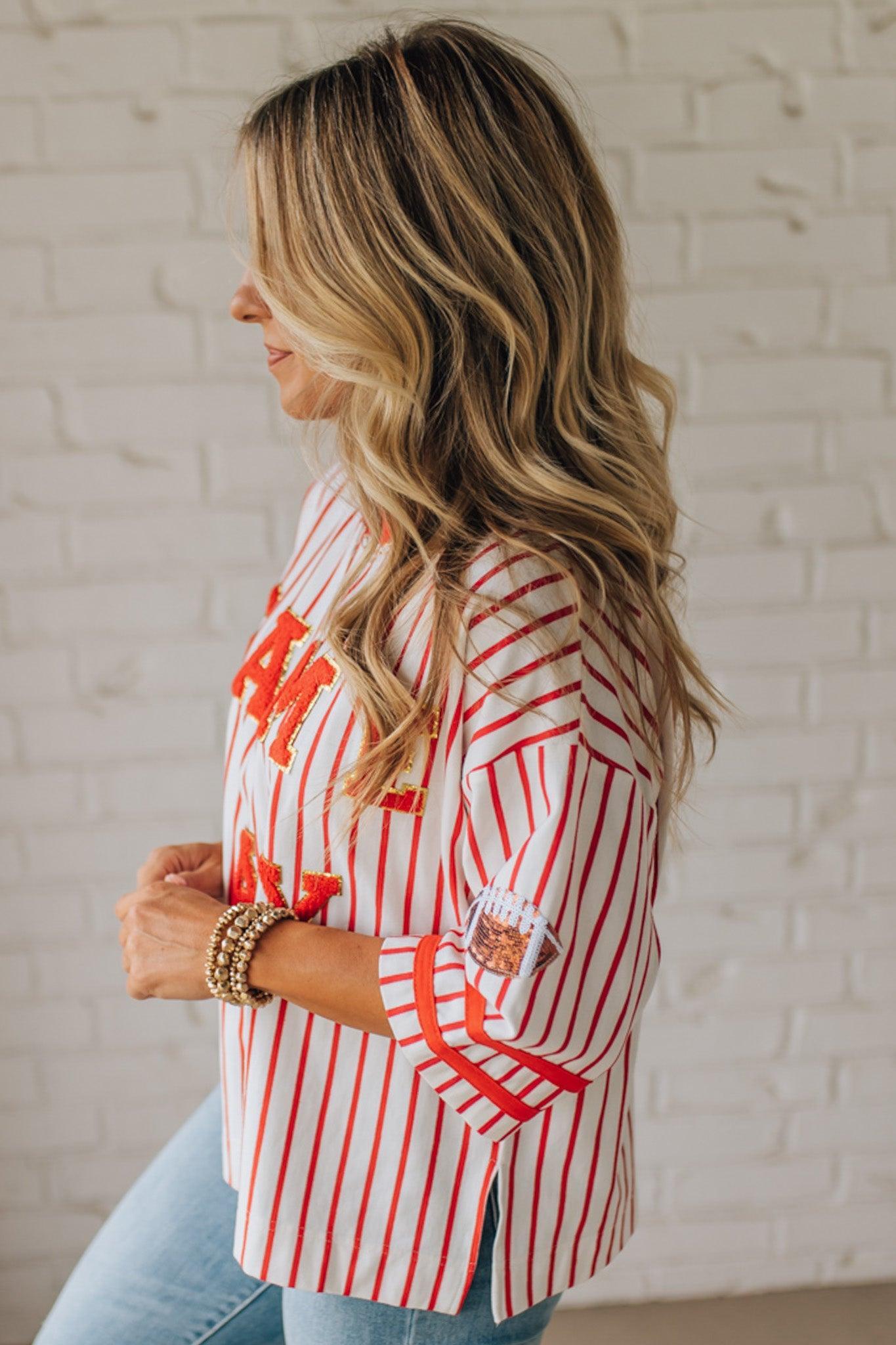Woman wearing a red and white striped shirt with rolled-up sleeves against a white brick wall.