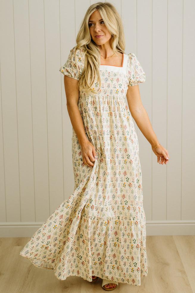 Woman wearing a floral dress against a plain wall.