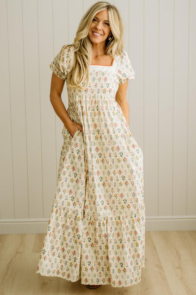Woman wearing a floral dress standing against a wooden paneled wall.