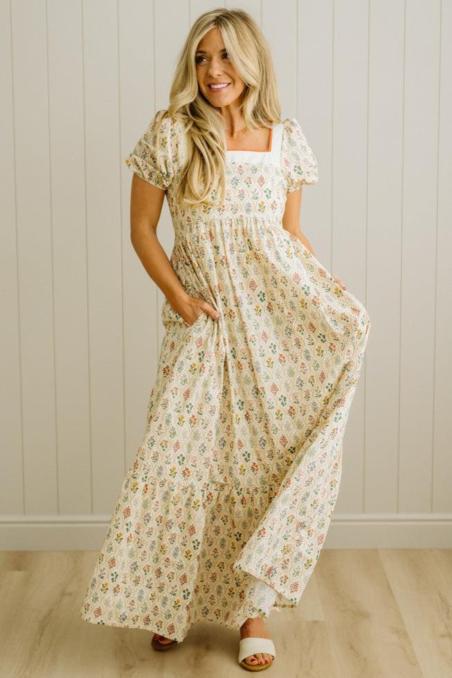 Woman wearing a floral dress standing against a plain wall.