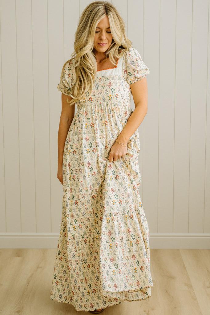 Woman wearing a floral dress standing against a plain wall.