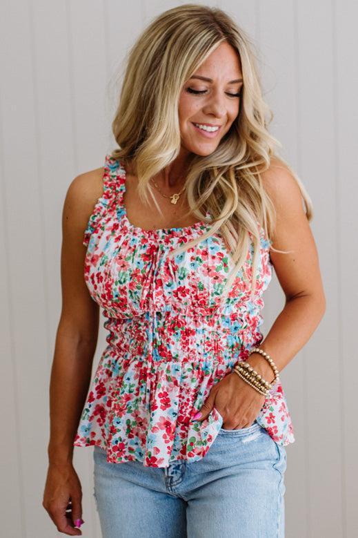 Woman wearing a floral sleeveless top and jeans against a plain background