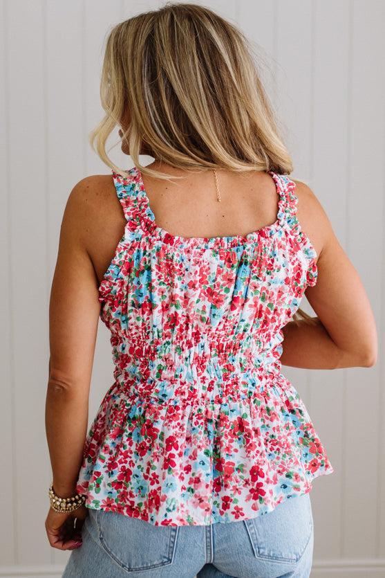 Woman wearing a floral sleeveless top and blue jeans against a neutral background