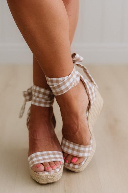 Woman wearing a mocha and cream gingham print wrap wedge sandals.