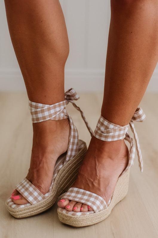 Woman wearing a mocha and cream gingham print wrap wedge sandals.