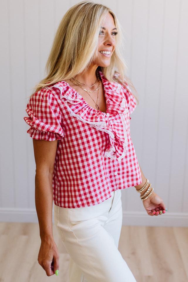 Woman wearing a red and white checkered blouse with ruffled details.