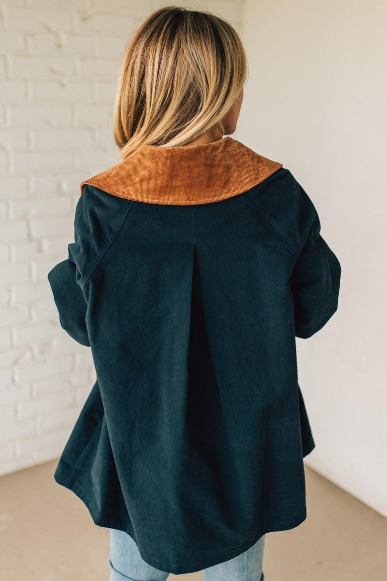 Person wearing a dark blue coat with a brown collar against a white brick wall.