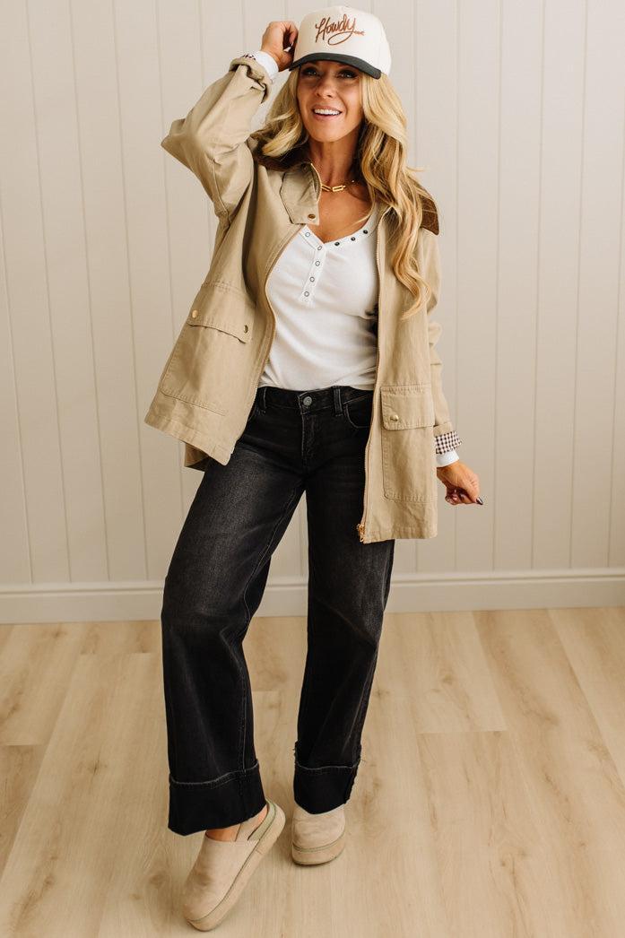 Woman wearing a beige jacket, white shirt, black pants, and beige shoes indoors.