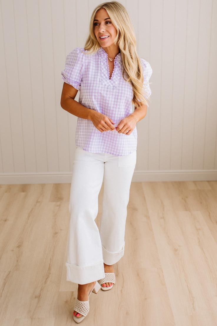 Blonde woman wearing a lavender and white gingham top with scallop edge trim and puff sleeves.