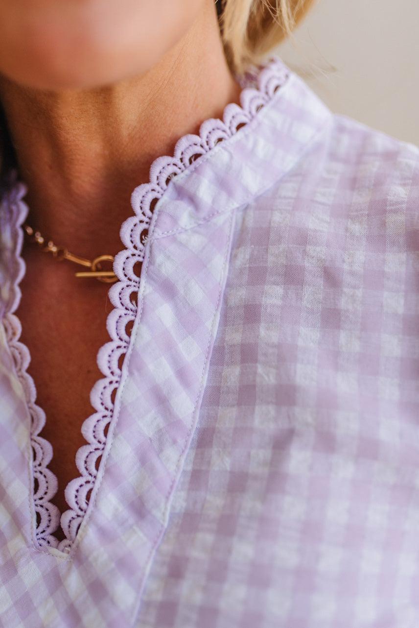 Blonde woman wearing a lavender and white gingham top with scallop edge trim and puff sleeves.